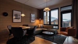 Una sala moderna con piso de madera, una mesa redonda de comedor, un sofá y dos sillones. Hay dos ventanas amplias con vistas al exterior.
