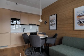 Eine moderne Küche mit Holzschränken, ein Essbereich mit rundem Tisch und Stühlen sowie ein grünes Sofa.