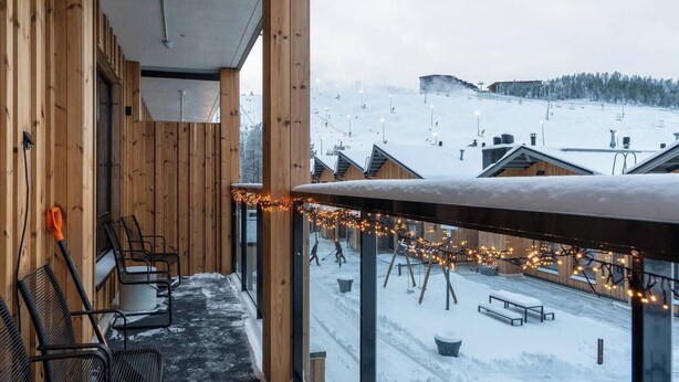 Un balcón de madera con sillas y vistas a una pista de esquí nevada.
