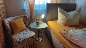 Une pièce chaleureuse avec un fauteuil à motifs floraux, une petite table ronde avec une lampe, un canapé avec des coussins et une fenêtre avec des rideaux.