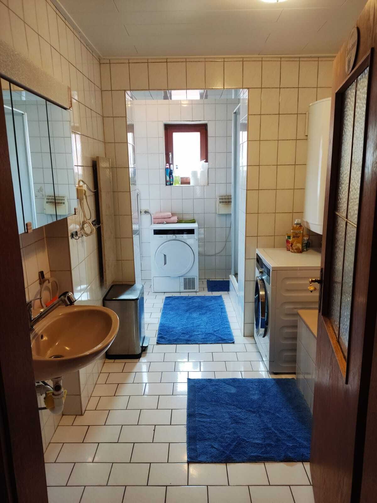 Pieni kylpyhuone, jossa on pesuallas, pesukone ja peili.