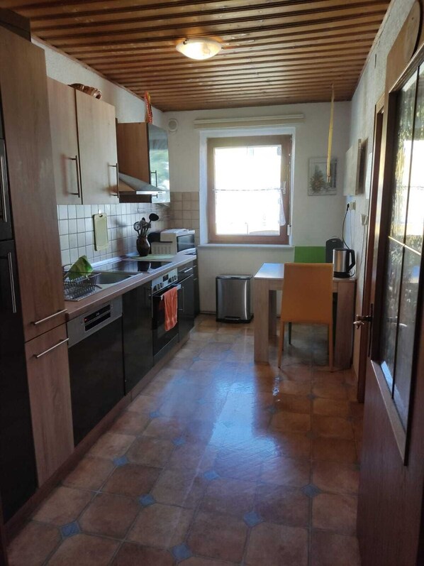 A compact kitchen with wooden cabinets, a tiled backsplash, a stainless steel refrigerator, a microwave, and a sink.