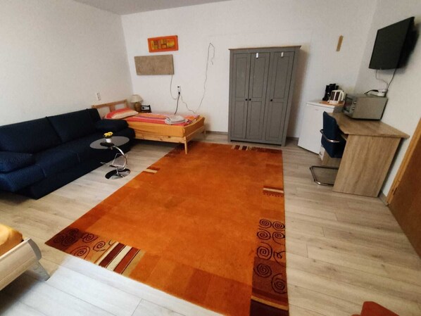 A living room with a sofa, a bed, a grey wardrobe, a television, and a small table with a lamp. - Müllers Monteurunterkunft Gangkofen (Gangkofen)