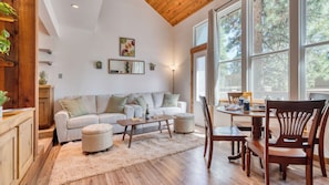 A cozy living room with a sofa, ottoman, coffee table, and wooden chairs.