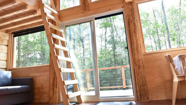 A wooden cabin interior with a loft bed, a sofa, and large windows offering a forest view. - Disconnect on a private estate, hiking trails, Finnish sauna, canoe,,,, (Saguenay)