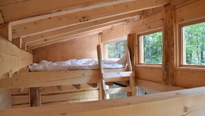 A cabin with a loft-style bedroom, wooden beams, and large windows offering a view of the forest. - Disconnect on a private estate, hiking trails, Finnish sauna, canoe,,,, (Saguenay)