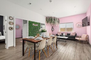 A modern living room with a dining area, pink walls, and a green wall with 'The Boutique' sign. - 8BR Nashville Group Stay - 5 Min to Downtown (Nashville)