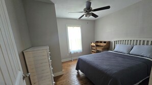 Een slaapkamer met een bed, een plafondventilator, een houten dressoir en een raam.