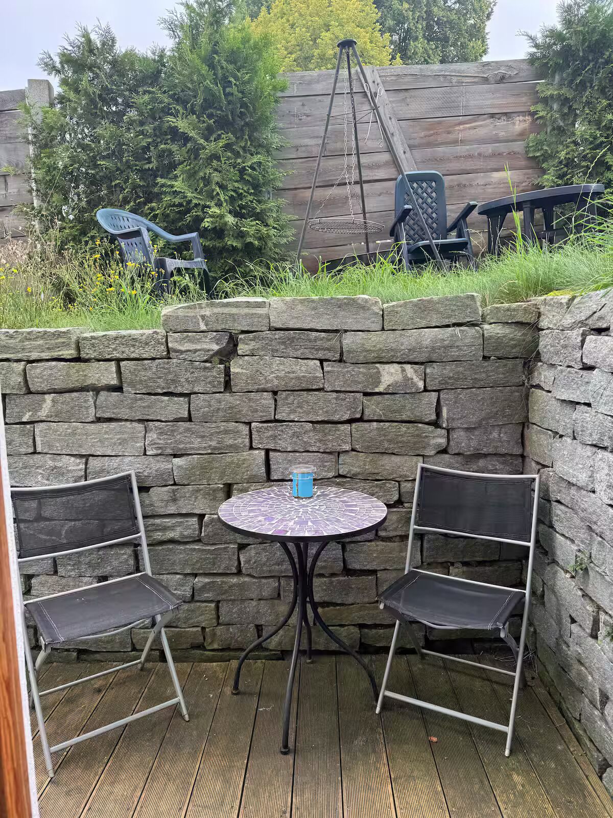 Eine steinerne Mauer mit einem kleinen runden Tisch und zwei Stühlen in einer Terrasse.