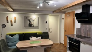 Ein kompakter Wohnbereich mit Küchenzeile, einem Essbereich mit Tisch und Stühlen, einer Couch und einem an der Wand hängenden Stiergemälde.