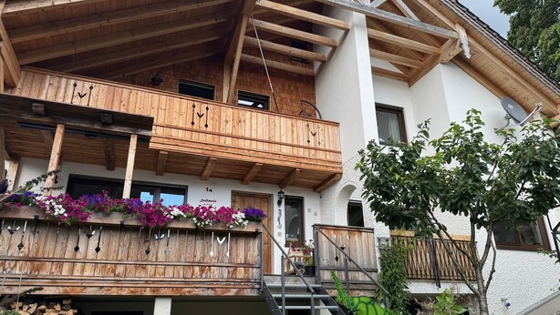 Eine Holzhütte mit Balkon, einer Treppe und einem Schild, das den Namen 'Sollemair' zeigt.