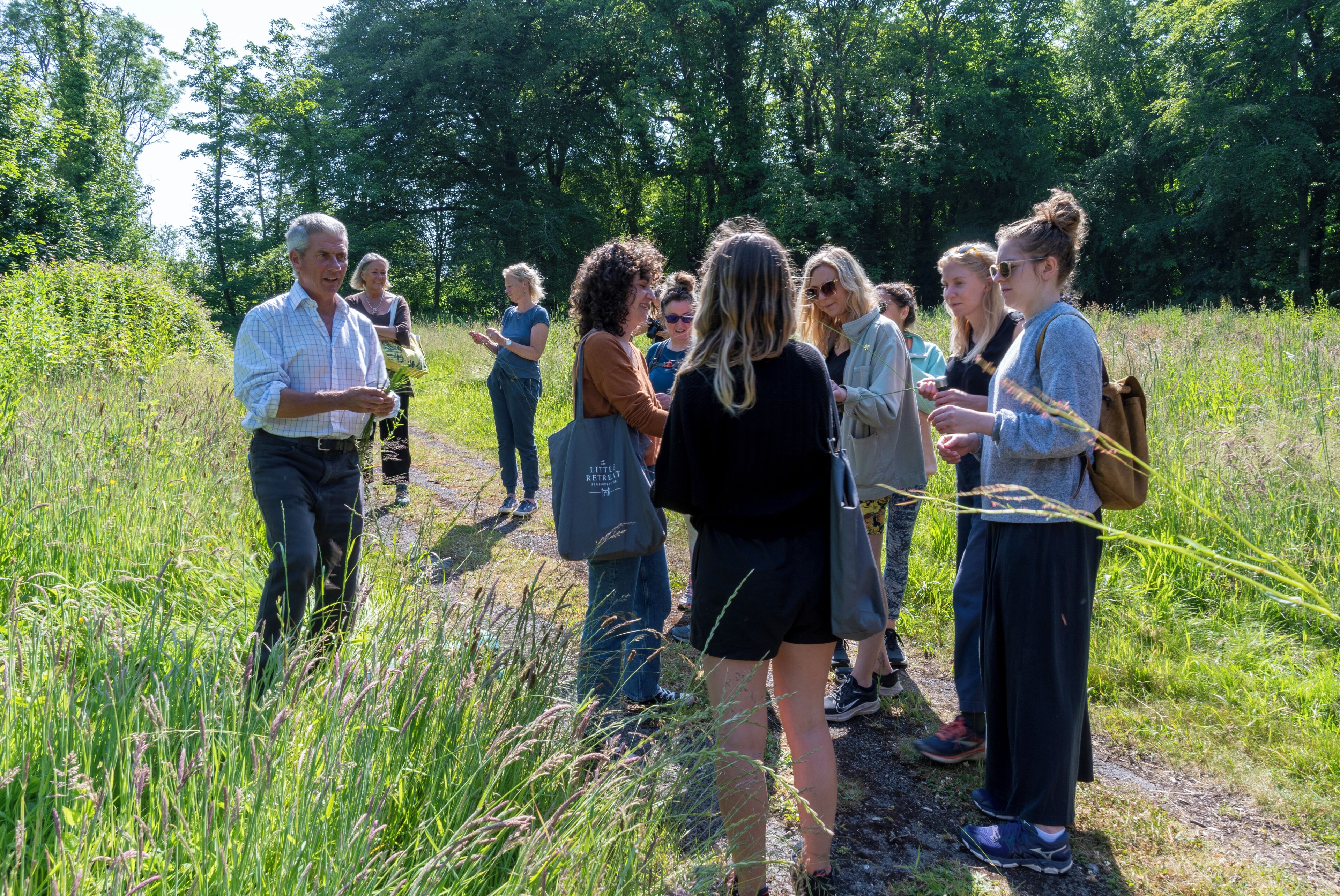 A group of people standing on a grassy path in a natural setting.