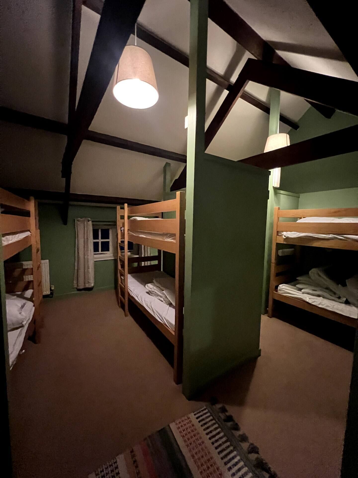 A room with bunk beds, a window with curtains, and a hanging light fixture.