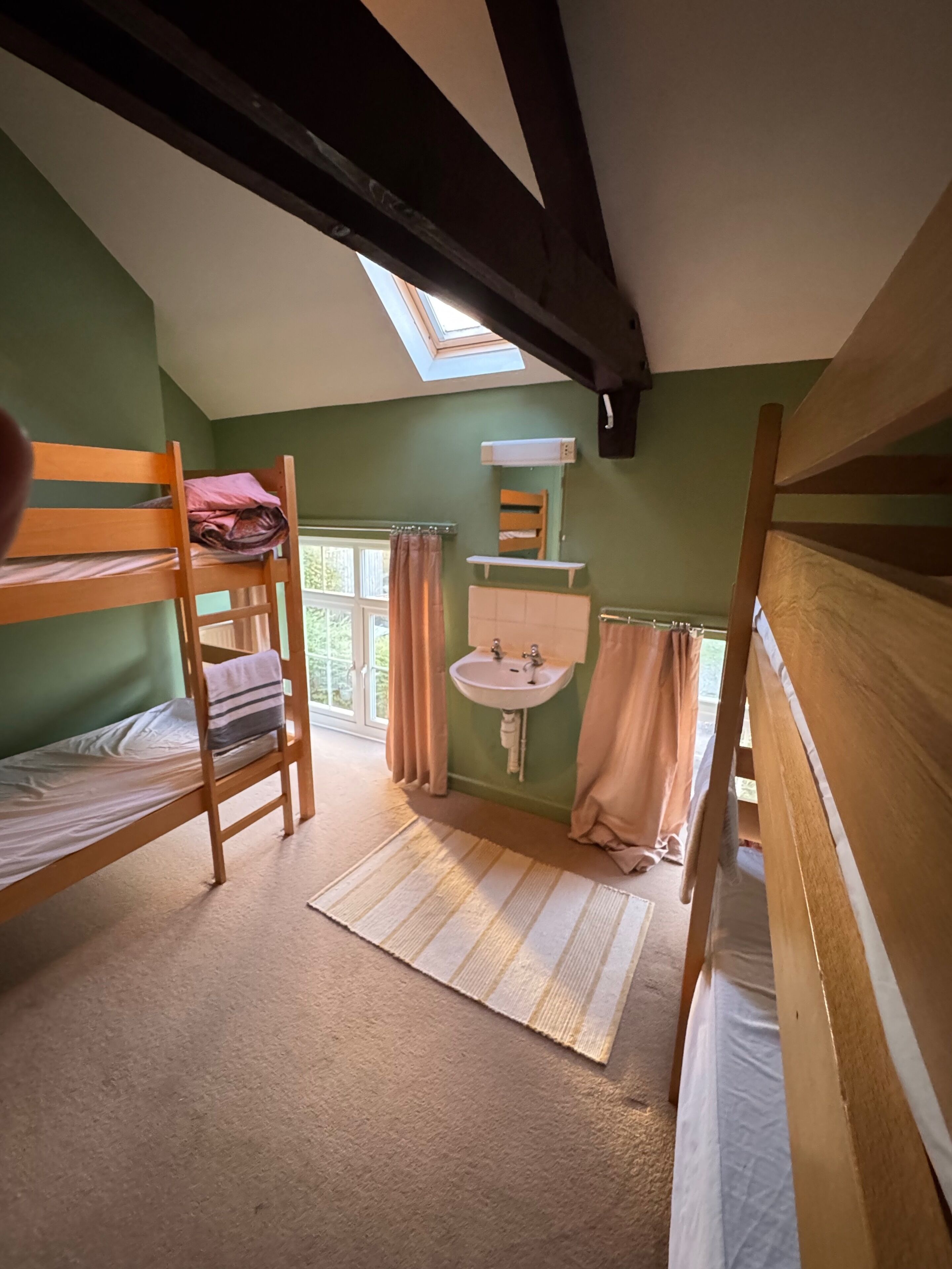 A dormitory room with bunk beds, a skylight, a window, a sink, and a mirror.
