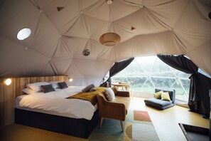 A spacious tent with a large bed, a sofa, and a dining area. - The Little Retreat (Kilgetty)