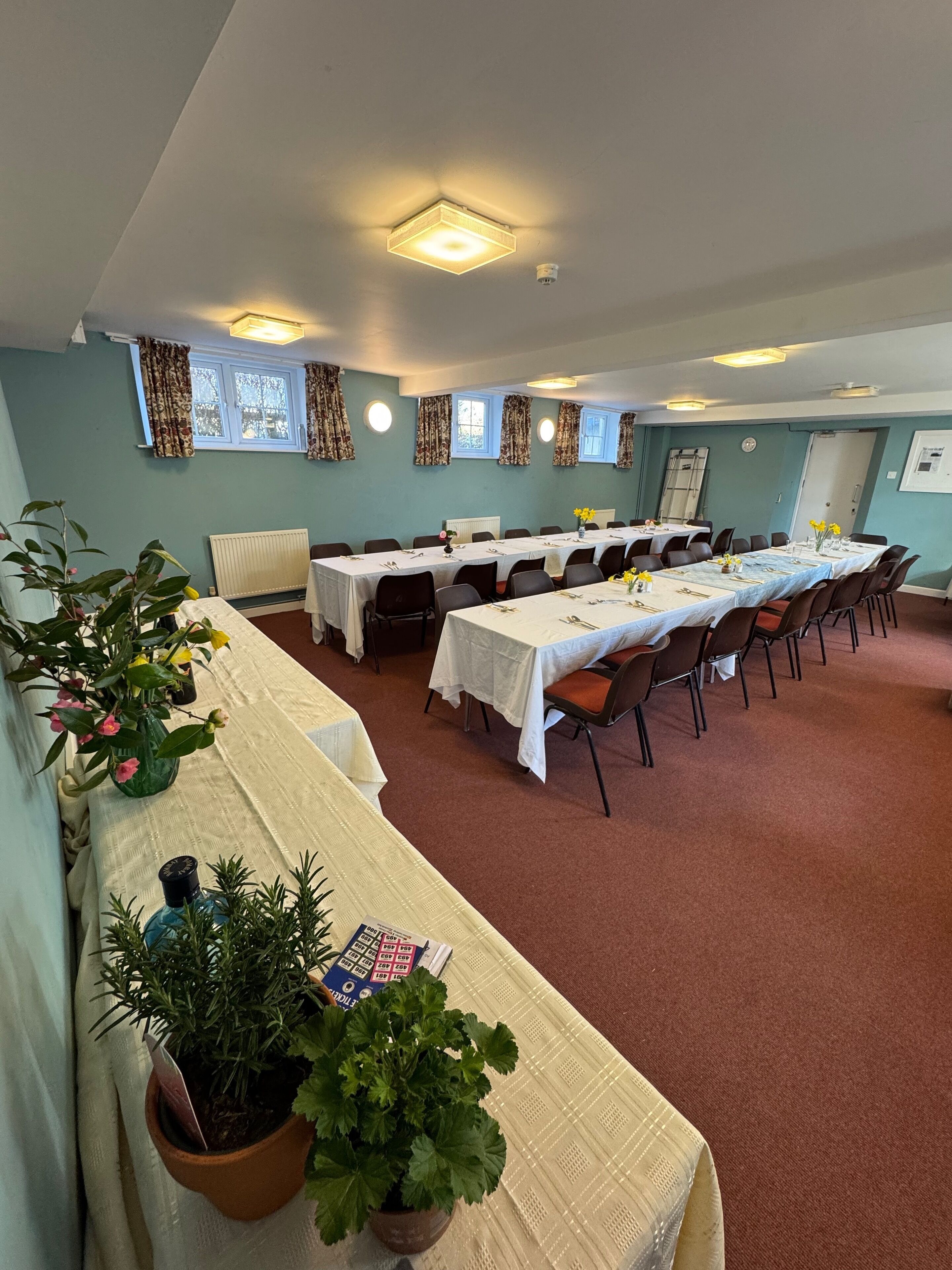 A conference room with long tables, chairs, and potted plants.