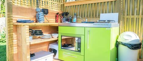 A compact outdoor kitchen with a built-in stove, storage cabinets, and a trash bin.
