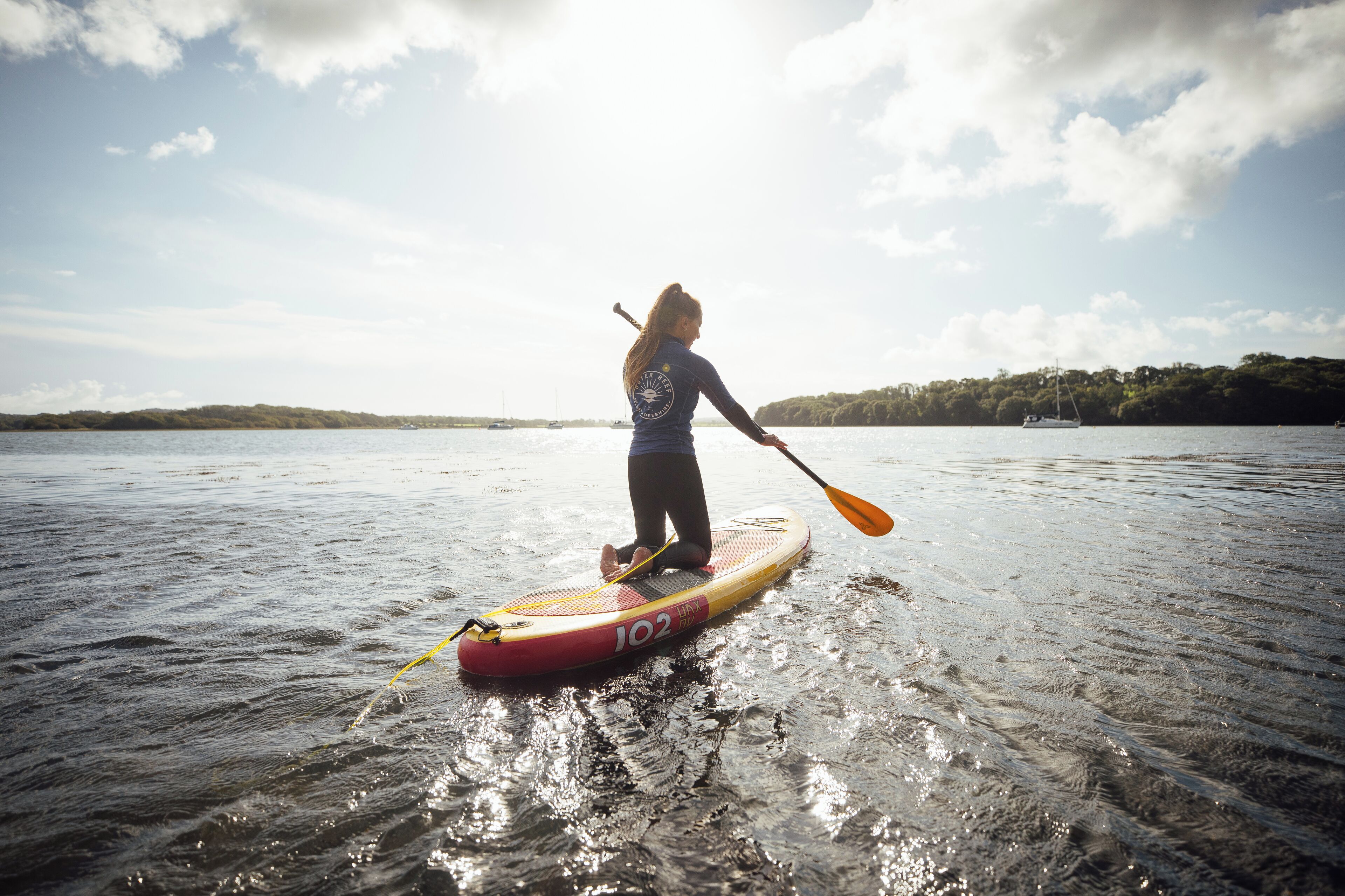 A person paddleboarding on a calm body of water with a clear sky.