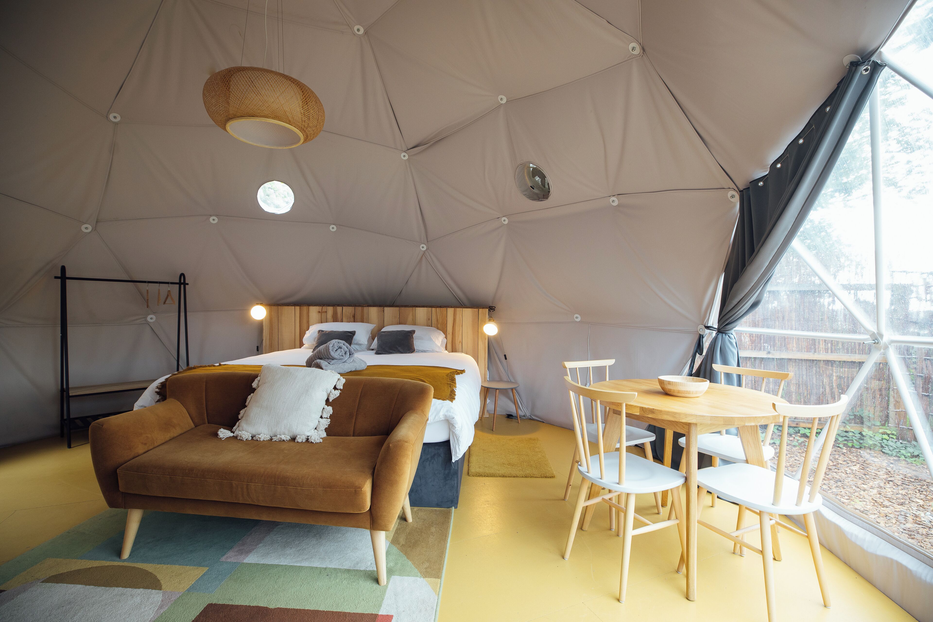 A tented accommodation with a bed, sofa, dining table, and chairs.