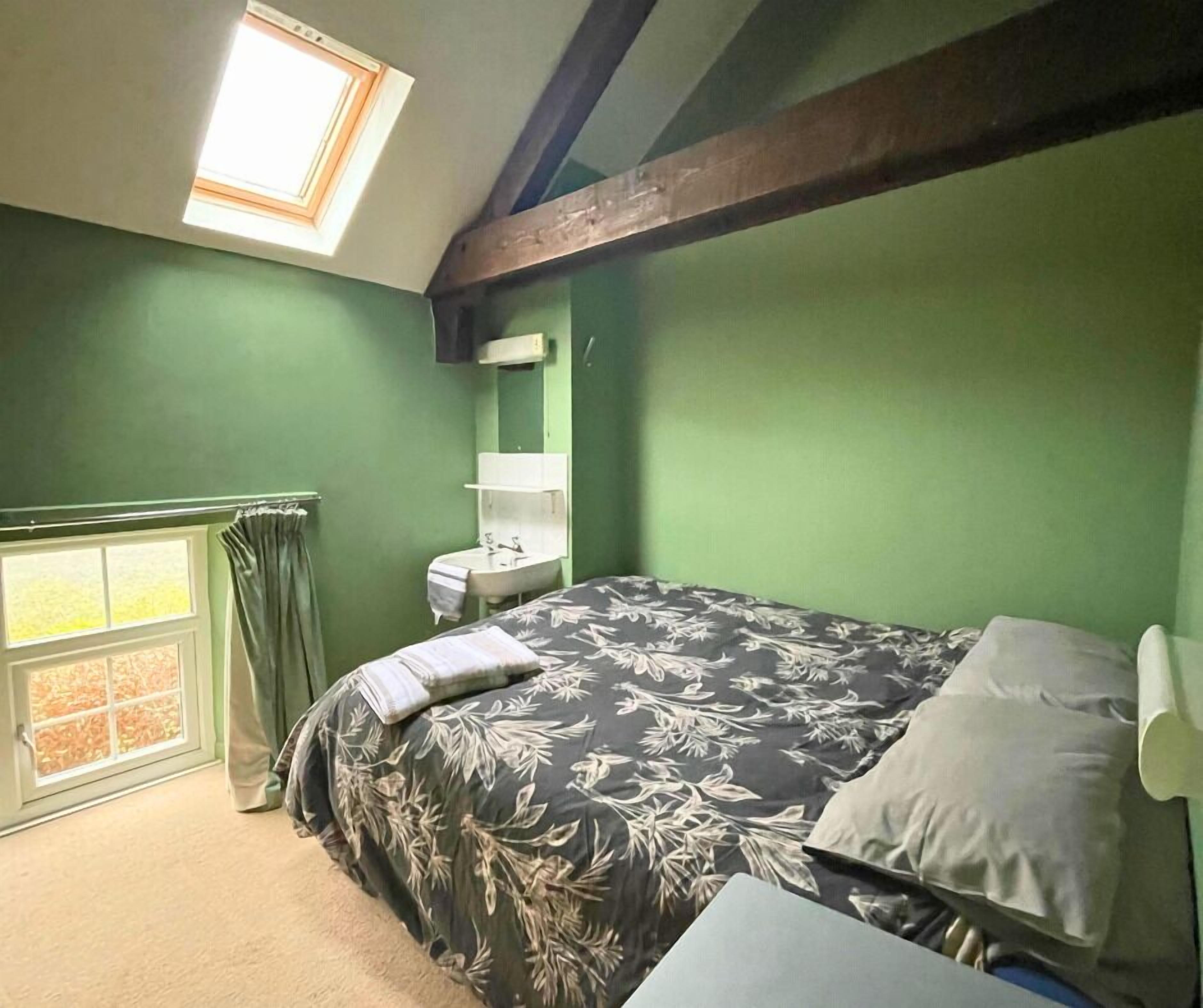 Una camera da letto con un lucernario, un letto con lenzuola a motivi floreali, un comodino e una finestra con tende.