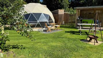 A geodesic dome structure in a backyard with a picnic table and chairs, surrounded by a wooden fence and greenery.