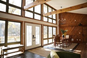 A spacious room with large windows, a wooden ceiling, and a dining area with chairs and a table.