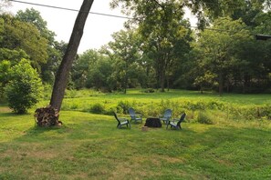 A grassy outdoor area with a pile of firewood, a table, and four chairs.