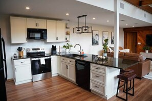 A modern kitchen with white cabinetry, a black stove, and a central island with stools.