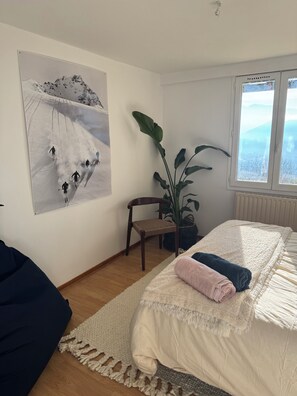A bedroom with a bed, a chair, a large plant, and a painting of a snowy mountain scene. - A modern home with breathtaking views (La Tronche)