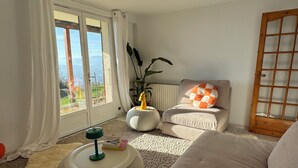 A living room with a sofa, ottoman, and a view through a glass door. - Modern nest with breathtaking views (La Tronche)
