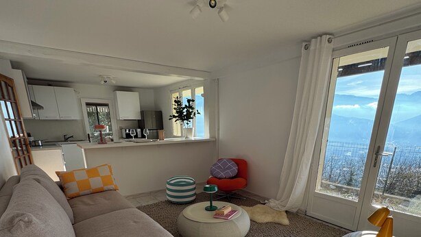 A modern living room with a sofa, ottoman, and a view of the mountains through a large window. - Modern nest with breathtaking views (La Tronche)
