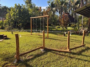 A wooden swing set in a grassy area with trees and a building in the background. - Sabalo lodge (Sierpe)