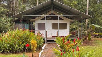 A small, white, tent-like structure with a metal roof, surrounded by lush greenery and various flowering plants.