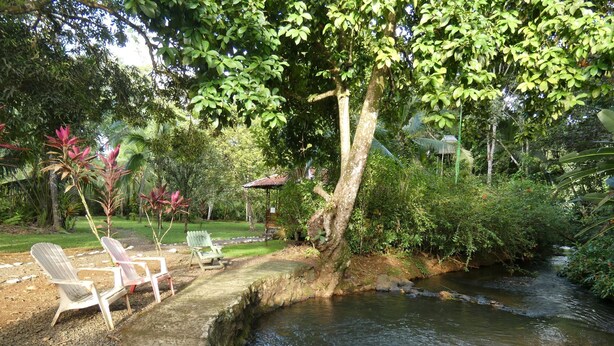 A serene outdoor area with a small stream, two wooden chairs, and lush greenery. - Sabalo lodge (Sierpe)