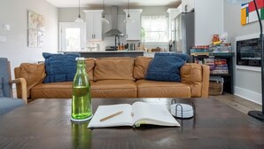 Ein Wohnzimmer mit einem braunen Ledersofa, einem offenen Buch, einer grünen Flasche und einer Lampe.
