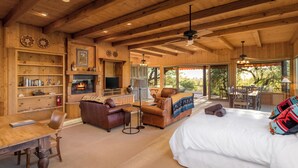 A spacious room with a wooden ceiling, a fireplace, a sofa, a bed, and a dining table.