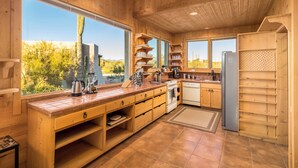 A wooden kitchen with large windows, a built-in oven, and a refrigerator.