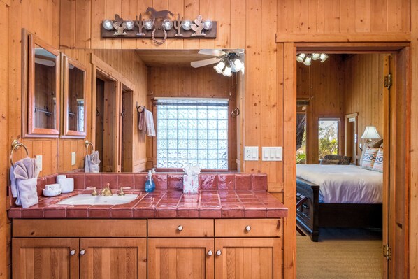 Une cabane en bois dotée d’une salle de bain comprenant un grand miroir, un lavabo et un ventilateur de plafond.
