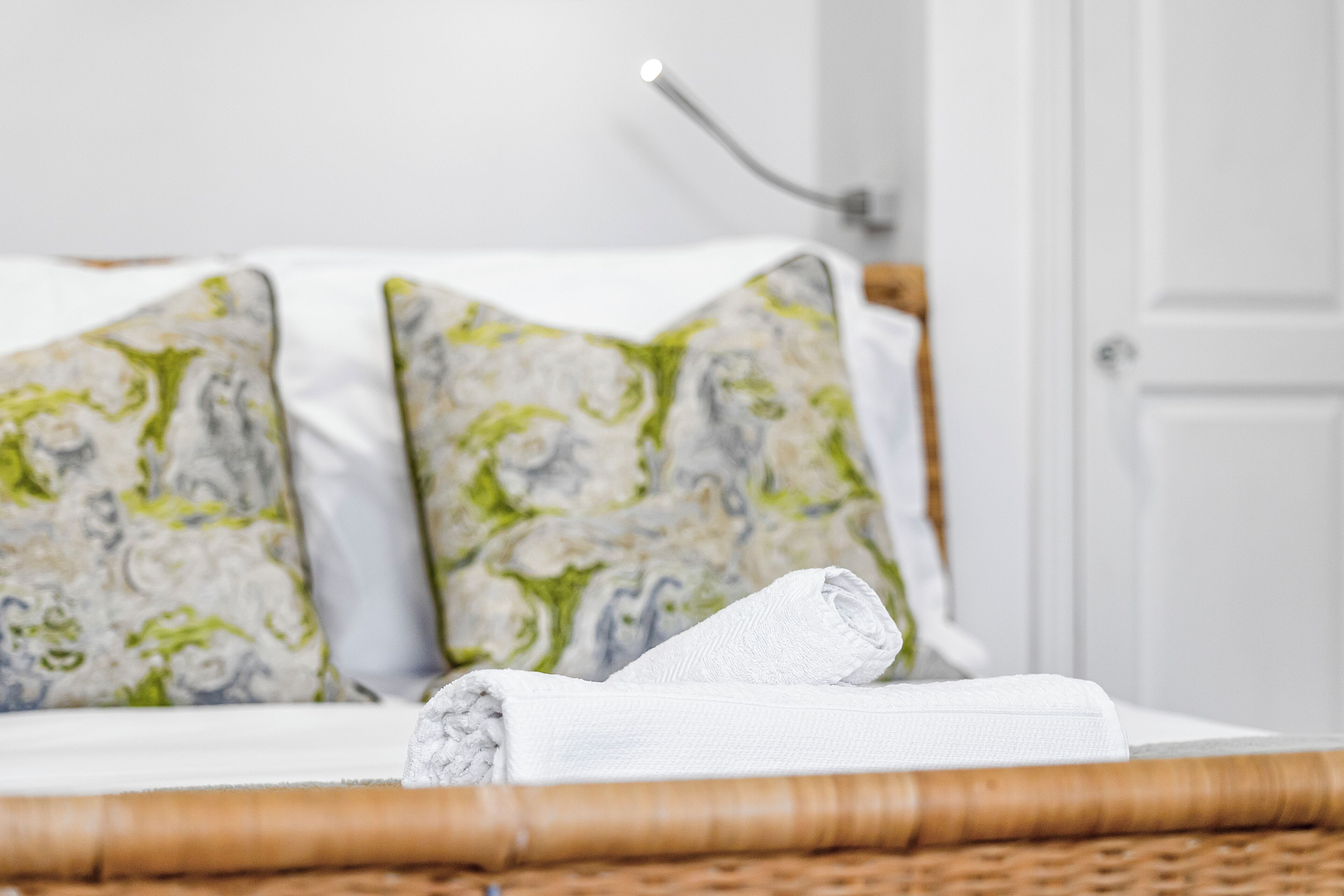 Een bed met een wit laken en twee kussens met een groen-wit patroon.