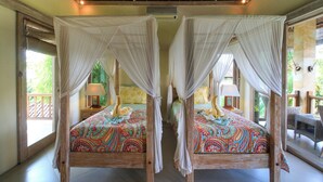 A room with two wooden four-poster beds with white canopies, colorful bedding, bedside lamps, and a view of greenery outside. - Brilliant 3-bedroom villa with Pool and AC in peaceful Ubud (Ubud)