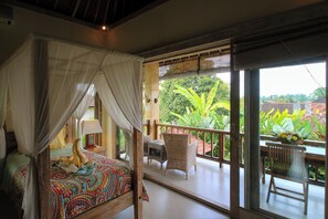 Ein Zimmer mit Himmelbett, einem Balkon mit Korbmöbeln und Blick auf üppige Grünflächen.