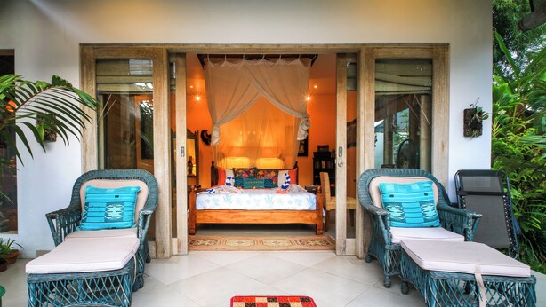 A room with a bed, two wicker chairs with cushions, a red and black checkered mat, and a large window. - Brilliant 3-bedroom villa with Pool and AC in peaceful Ubud (Ubud)