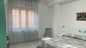 A bedroom with a bed, a chair, a curtain, and a wall decoration. - Just minutes from Ogliastra's most beautiful beaches, rooms with en suite facilities (Cardedu)