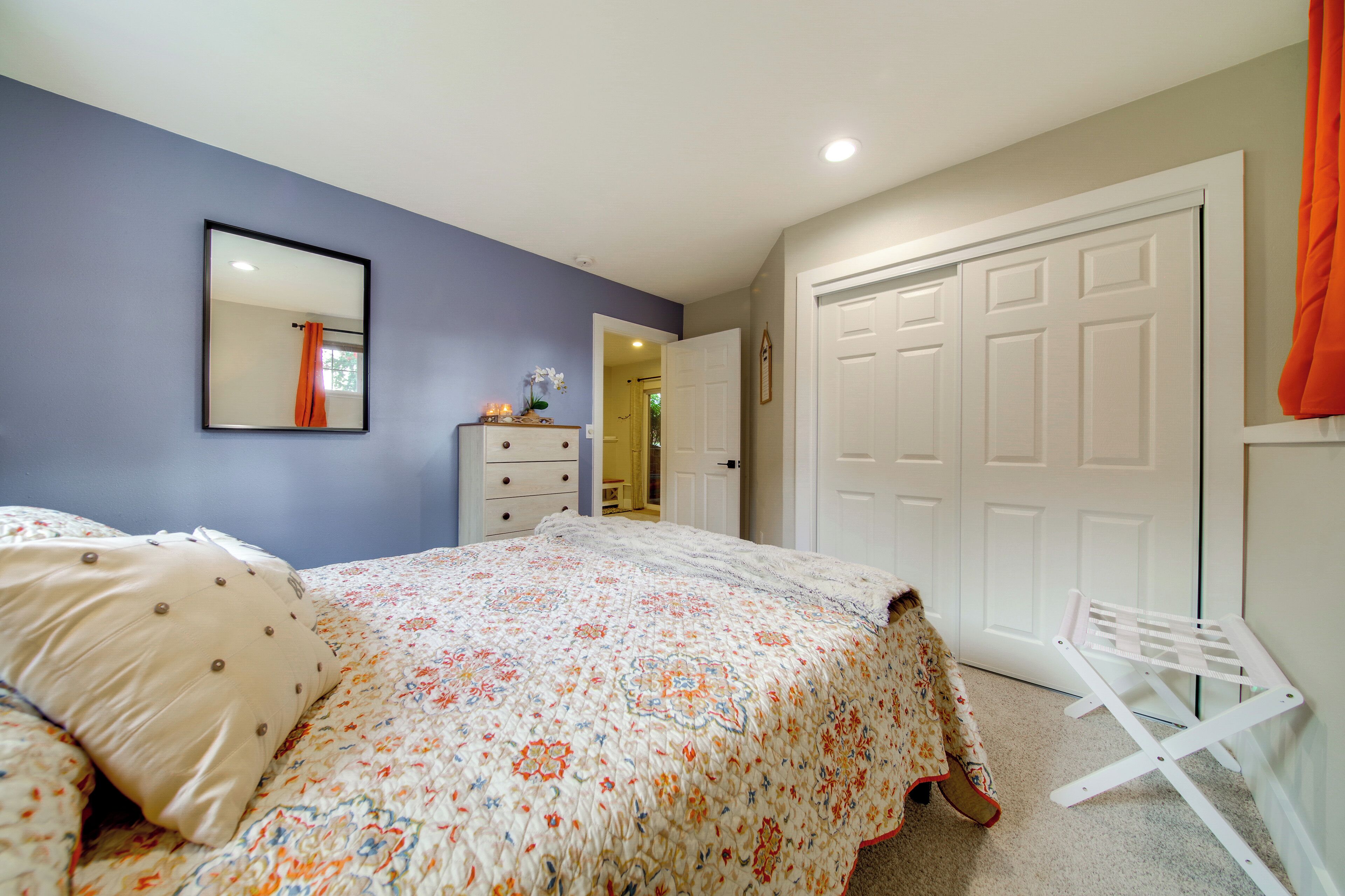 Un dormitorio con cama, cómoda, espejo y una puerta que da a otra habitación.