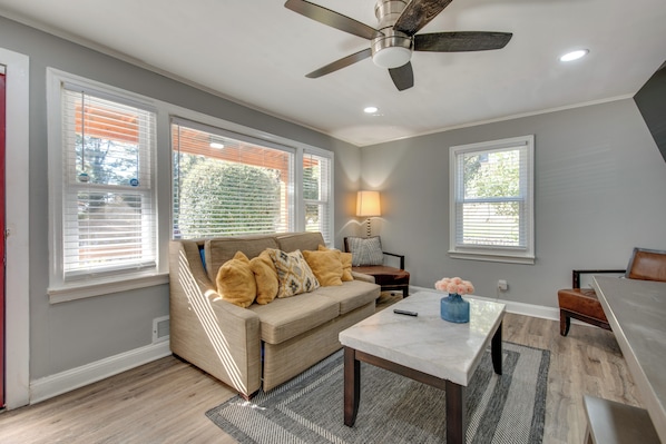 A living room with a beige sofa, a coffee table, and a ceiling fan. - 5 Mi to Dtwn ATL! Cutest Cottage in Venetian Hills (Atlanta)