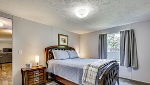 Ein Schlafzimmer mit einem hölzernen Bett, einem Nachttisch mit Lampe, einem gerahmten Bild an der Wand und einem Fenster mit Vorhängen.