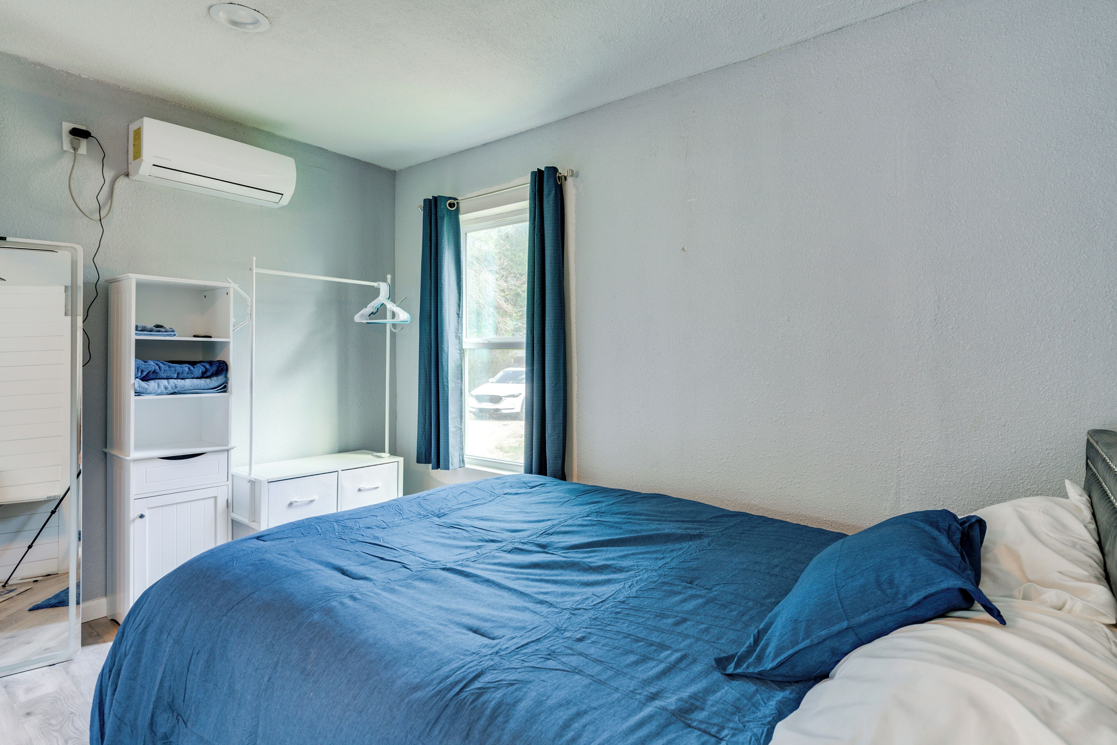 A bedroom with a bed, a wardrobe, a desk, and a window with curtains.