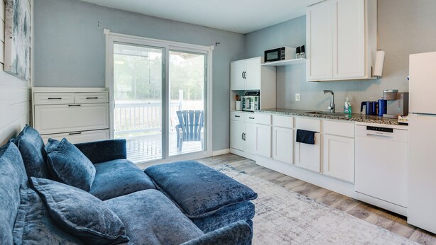 A modern kitchen with white cabinets, a microwave, and a dishwasher. There is a blue couch with pillows in the living area. - 10 Mi to Lake Conroe: Couple’s Retreat w/ Porch! (Montgomery)