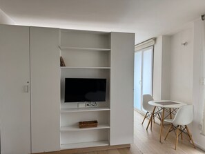 A modern living space with a built-in TV, white shelving, a dining area with a table and chairs, and a large window. - Beautiful Apartment in the Heart of Downtown D20 (Mexico City)