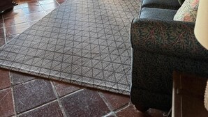Ein Wohnzimmer mit einem gemusterten Teppich, einem blauen Sofa mit gemusterten Kissen und einer Treppe, die zu einem Außenbereich führt.